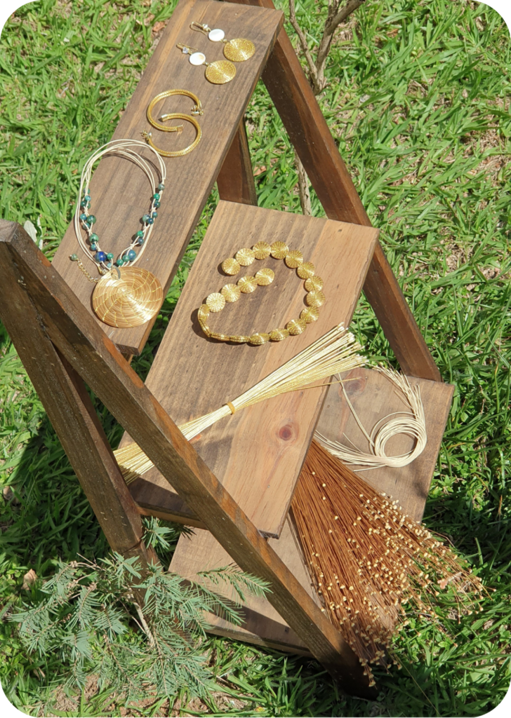 Escadinha com matérias primas Prateleira que mostra Biojóias de Capim Dourado e a matéria prima: colar de mandala e brincos de argola